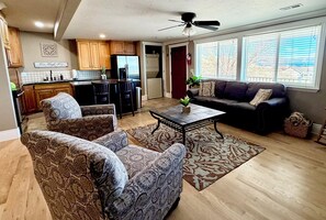 A modern living room with a sofa, two armchairs, a coffee table, and a ceiling fan.