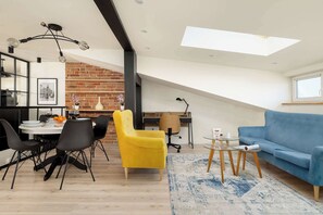 Moderni loft-tyylinen asunto, jossa on ruokailutila, sininen sohva ja tiiliseinä.