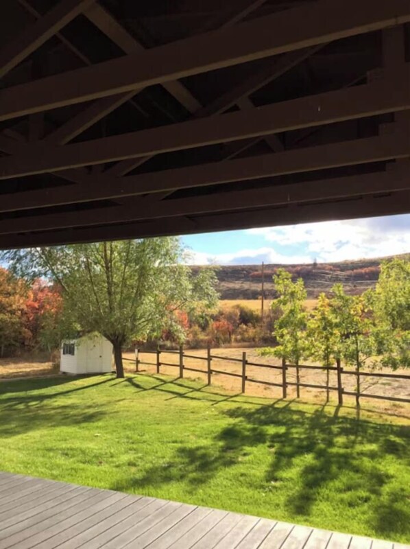 A view from a covered outdoor area with a wooden deck, a fenced yard, and a small white building.