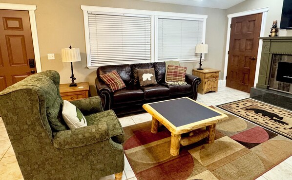 A living room with a brown leather sofa, a green armchair, a wooden coffee table, and a fireplace.