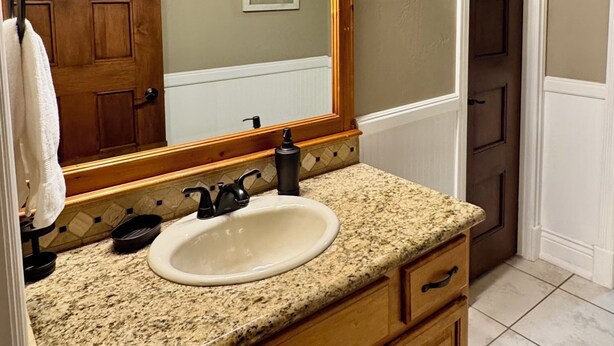 A bathroom with a granite countertop, a white sink, wooden cabinets, a large mirror, and a wall-mounted light fixture. - Boat parking | Hot Tub |  Sports Crt | Views (Garden City)