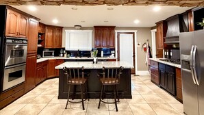Una cocina con detalles en pared de piedra, armarios de madera, una isla central con taburetes de bar y electrodomésticos de acero inoxidable.
