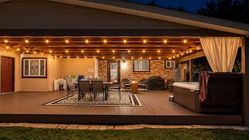 A covered outdoor patio with string lights, a barbecue grill, and a hot tub.