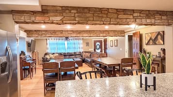 A spacious kitchen with granite countertops, a dining area with a wooden table and chairs, a stone accent wall, and a living room with a sofa and a fireplace.