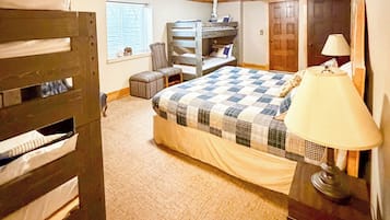 A bedroom with a bunk bed, a chair, a bedside table with a lamp, a window with blinds, and a door.