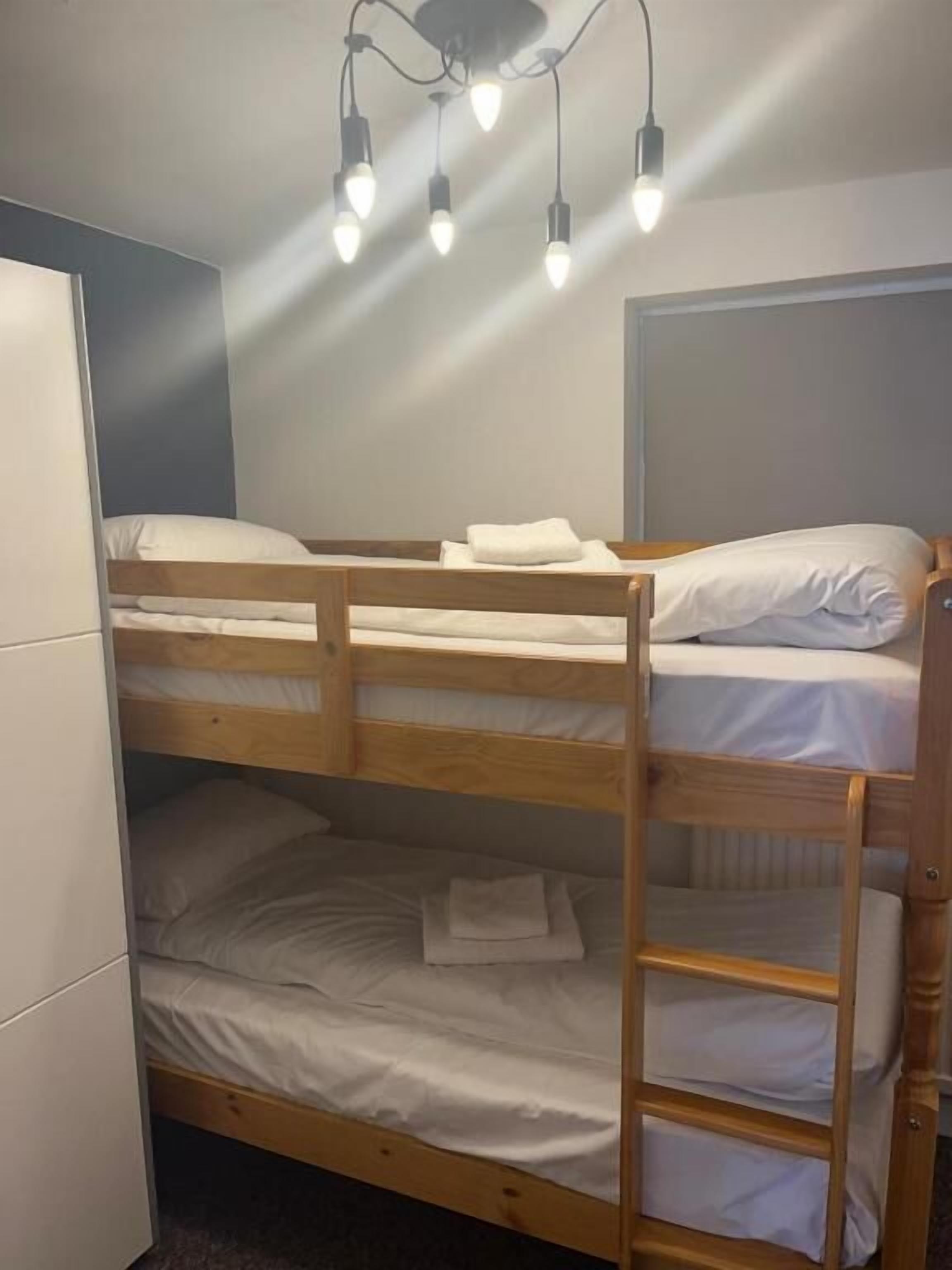 A bunk bed with a wooden frame, white bedding, and a ceiling light fixture.