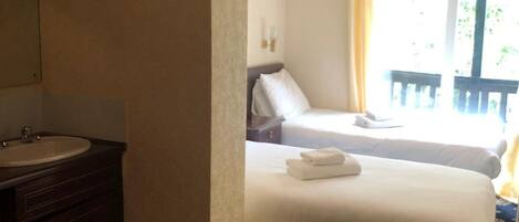 Una habitación de hotel con cama, baño con lavamanos y balcón con barandilla.
