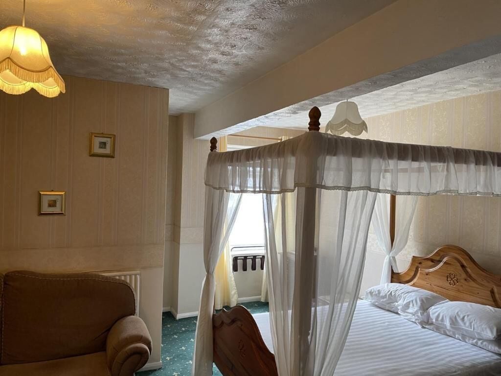 A room with a four-poster bed, a sofa, and a ceiling light fixture.
