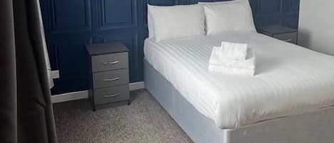 Un dormitorio con una cama grande, una mesita de noche, un aparador y una pared azul con textura.