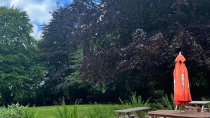 An outdoor patio with wooden tables and chairs, surrounded by greenery and trees. - Moorville Hall Hotel (Stoke-on-Trent)