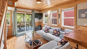 Ein gemütliches Blockhaus-Interieur mit Holzbalkendecke, einer Sofagarnitur, einem Esstisch und einem Kamin.
