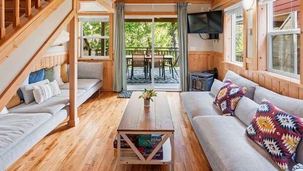 Ein gemütliches Blockhauss-Interieur mit einer Holztreppe, einer Couch, einem Couchtisch mit einer Vase und einem an der Wand montierten Fernseher.