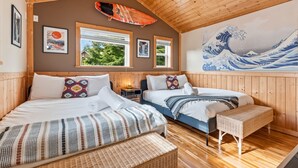 Ein Zimmer mit Holzwänden, zwei Betten, einem an der Wand befestigten Surfbrett, gerahmten Kunstwerken und einem großen Gemälde einer Welle.