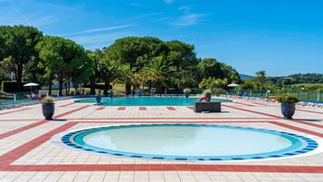 A swimming pool with a tiled deck, surrounded by palm trees and a clear sky.