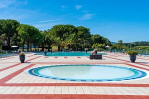 A swimming pool with a tiled deck, surrounded by palm trees and a clear sky.