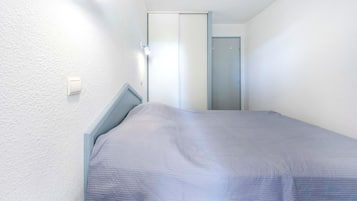 A small, narrow room with a single bed, a door, and a light fixture on the wall.