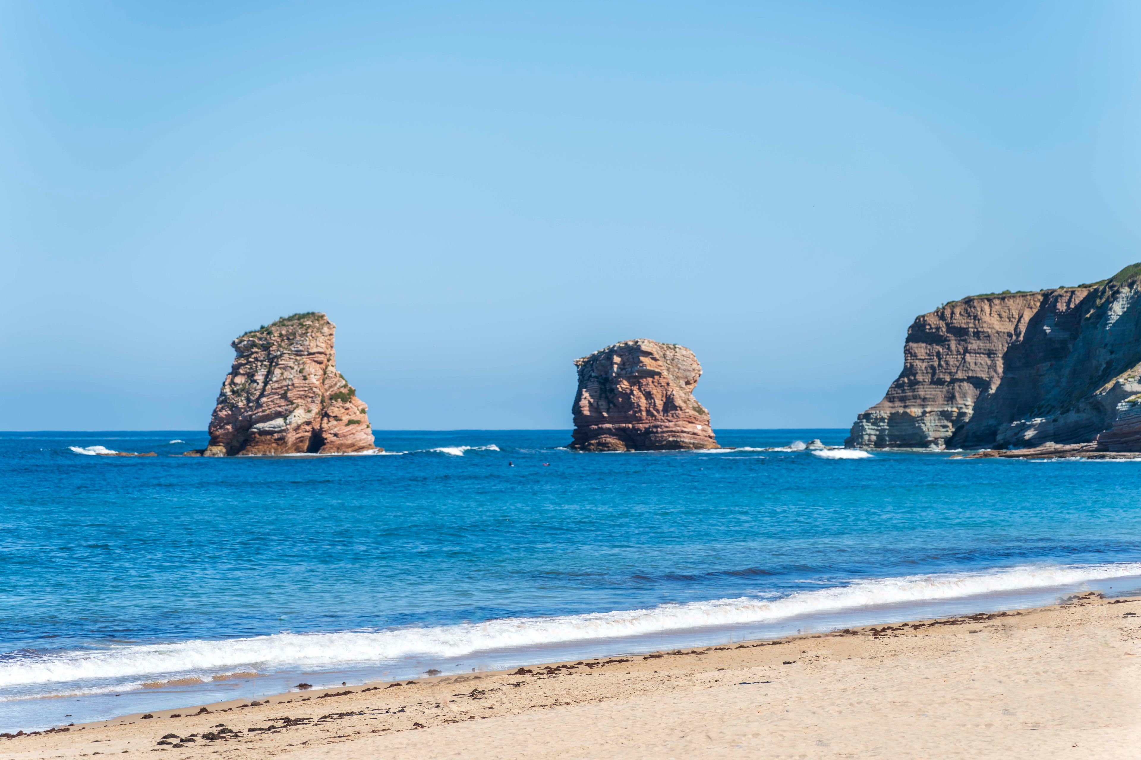 A beach with clear blue water and rocky formations.