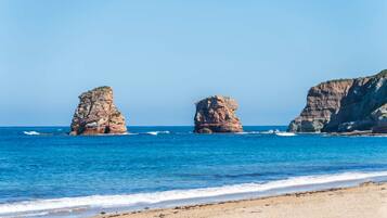 A beach with clear blue water and rocky formations.