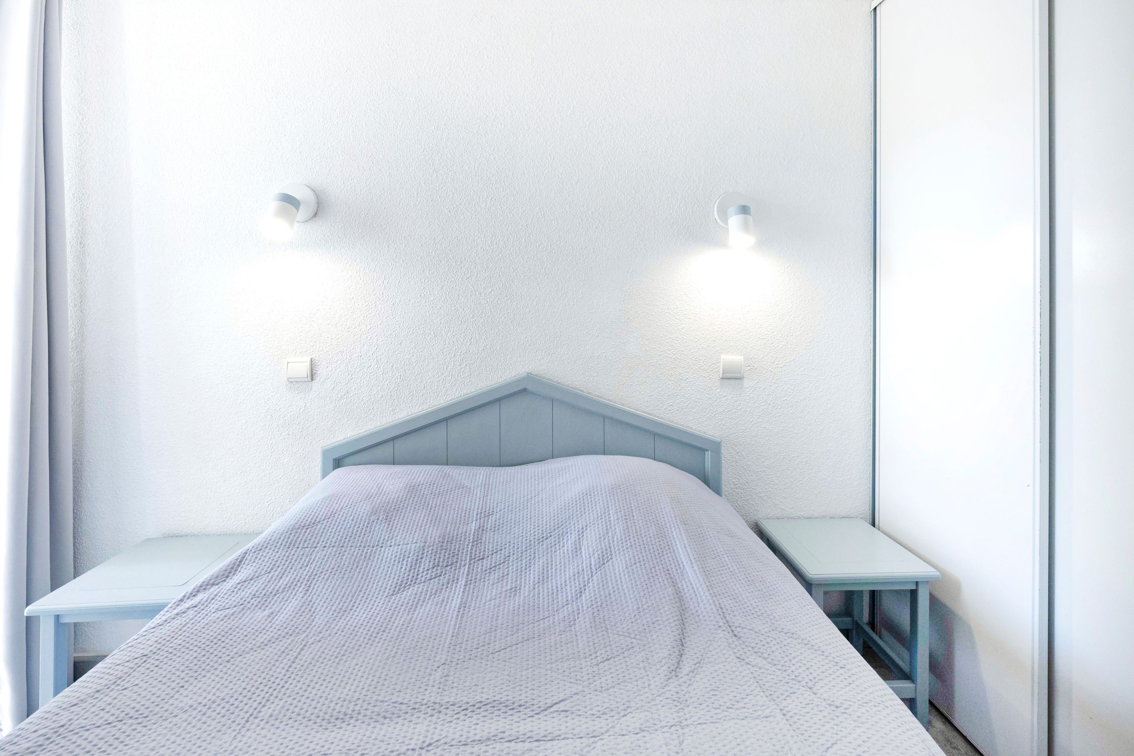 Un dormitorio con una cama individual, una mesita de noche y dos luces fijadas a la pared.