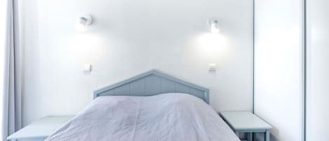 Quarto com uma cama de solteiro, mesa de cabeceira e duas luzes fixadas na parede.
