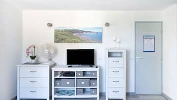 Una habitación con un escritorio blanco, un televisor de pantalla plana, una planta pequeña en maceta, un cuadro colgado en la pared y una puerta con un aviso.
