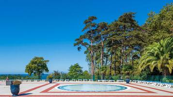 Ein Poolbereich mit rundem Pool, Liegestühlen und Blick auf das Meer.