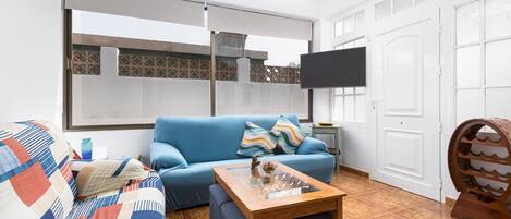 A living room with a blue sofa, a glass coffee table, and a TV on the wall.