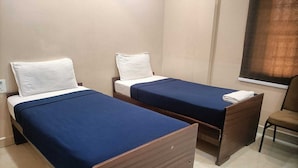 Une chambre d’hôtel avec deux lits simples, une table de chevet en bois, une chaise et une fenêtre avec des rideaux.
