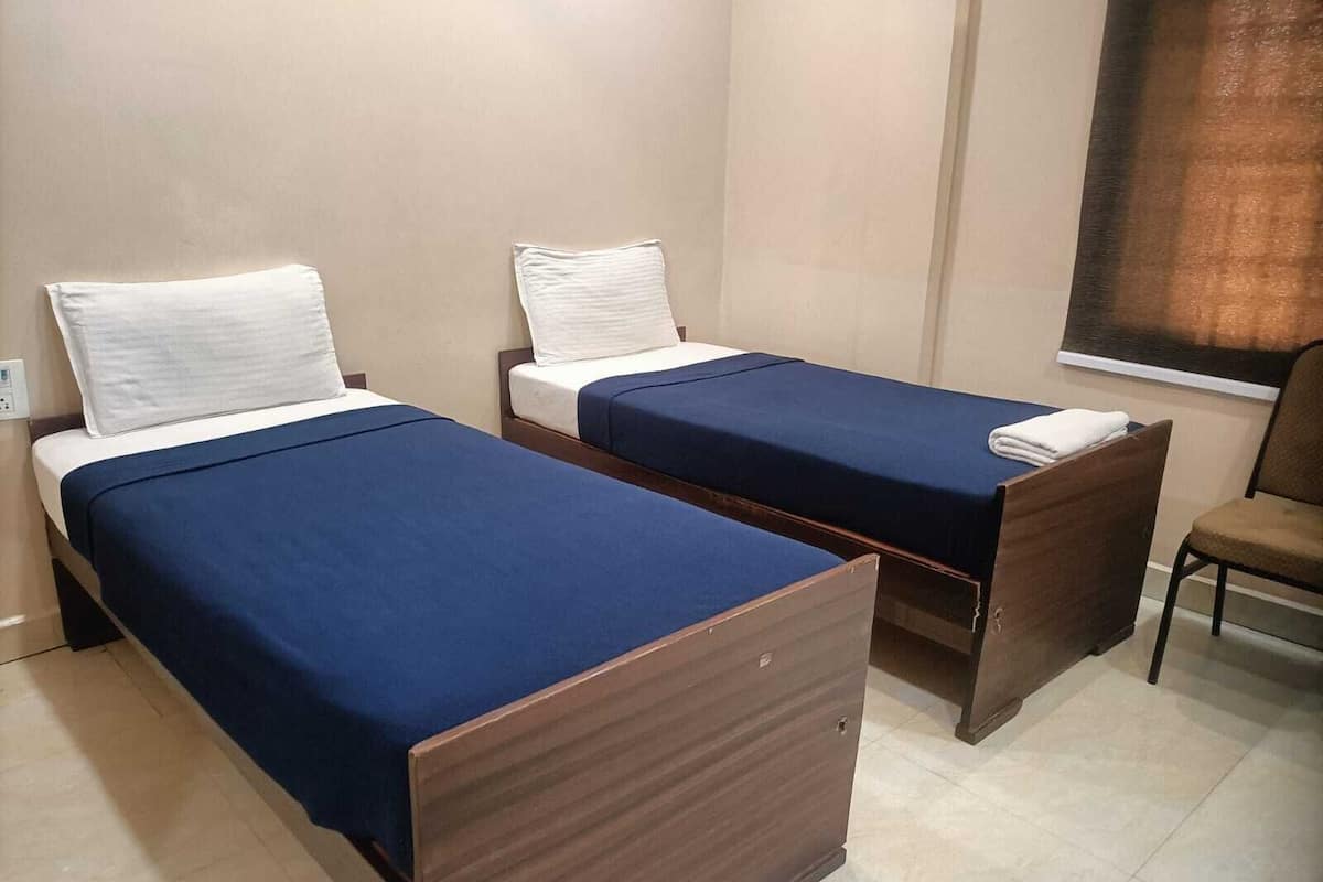 Habitación de hotel con dos camas individuales, una mesita de noche de madera, una silla y un ventanal con cortinas.