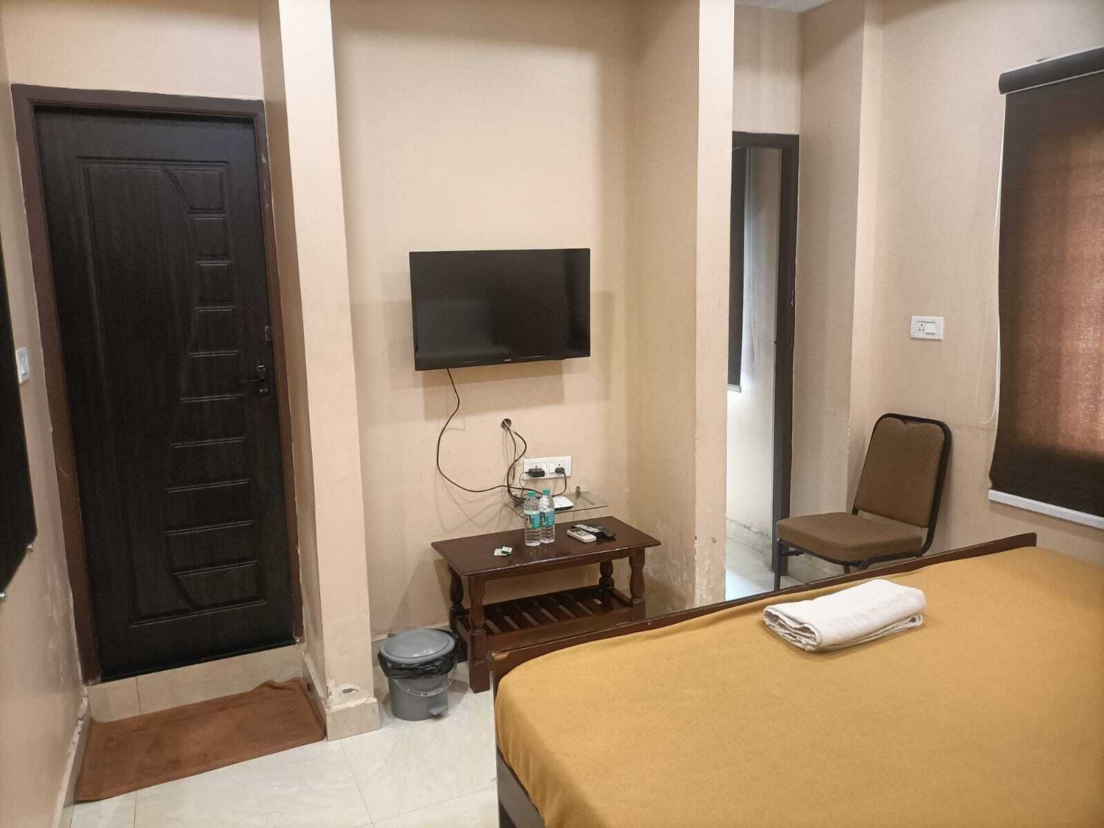 A hotel room with a bed, a television mounted on the wall, a small table with a trash bin, and a chair.