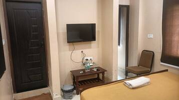 A hotel room with a bed, a television mounted on the wall, a small table with a trash bin, and a chair.