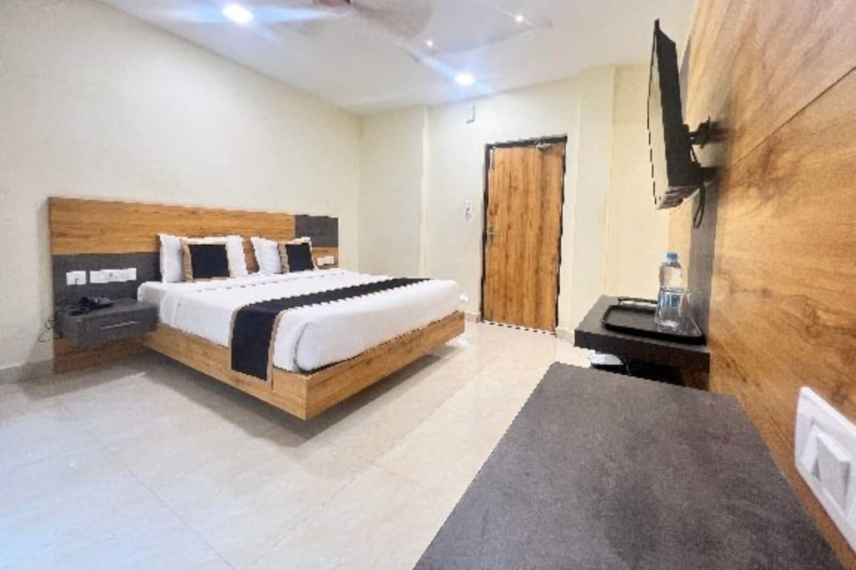 Un dormitorio con una cama de madera, una mesita de noche, un escritorio con silla, un televisor y un armario de madera.