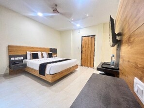 A bedroom with a wooden bed, a nightstand, a desk with a chair, a television, and a wooden wardrobe. - The Chiraag Inn (Chennai)