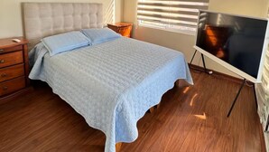 A bedroom with a bed, a dresser, a TV, and a window with blinds. - South Beach Front Apartment (Antofagasta)