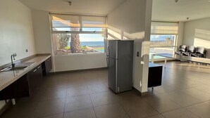 A modern kitchen with a large window, a refrigerator, and a dining area with chairs. - South Beach Front Apartment (Antofagasta)