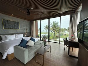 A modern hotel room with a large bed, a sofa, a TV, and a balcony with a view of the beach and palm trees. - Wyndham Hoi An Royal Beachfront Resort (Hoi An)