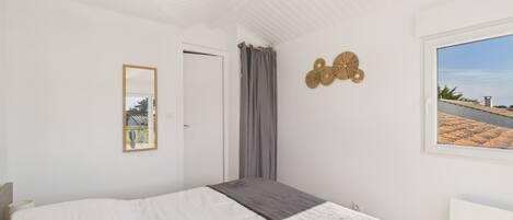 A bedroom with a bed, a window with a view, a door, and a wall decoration.