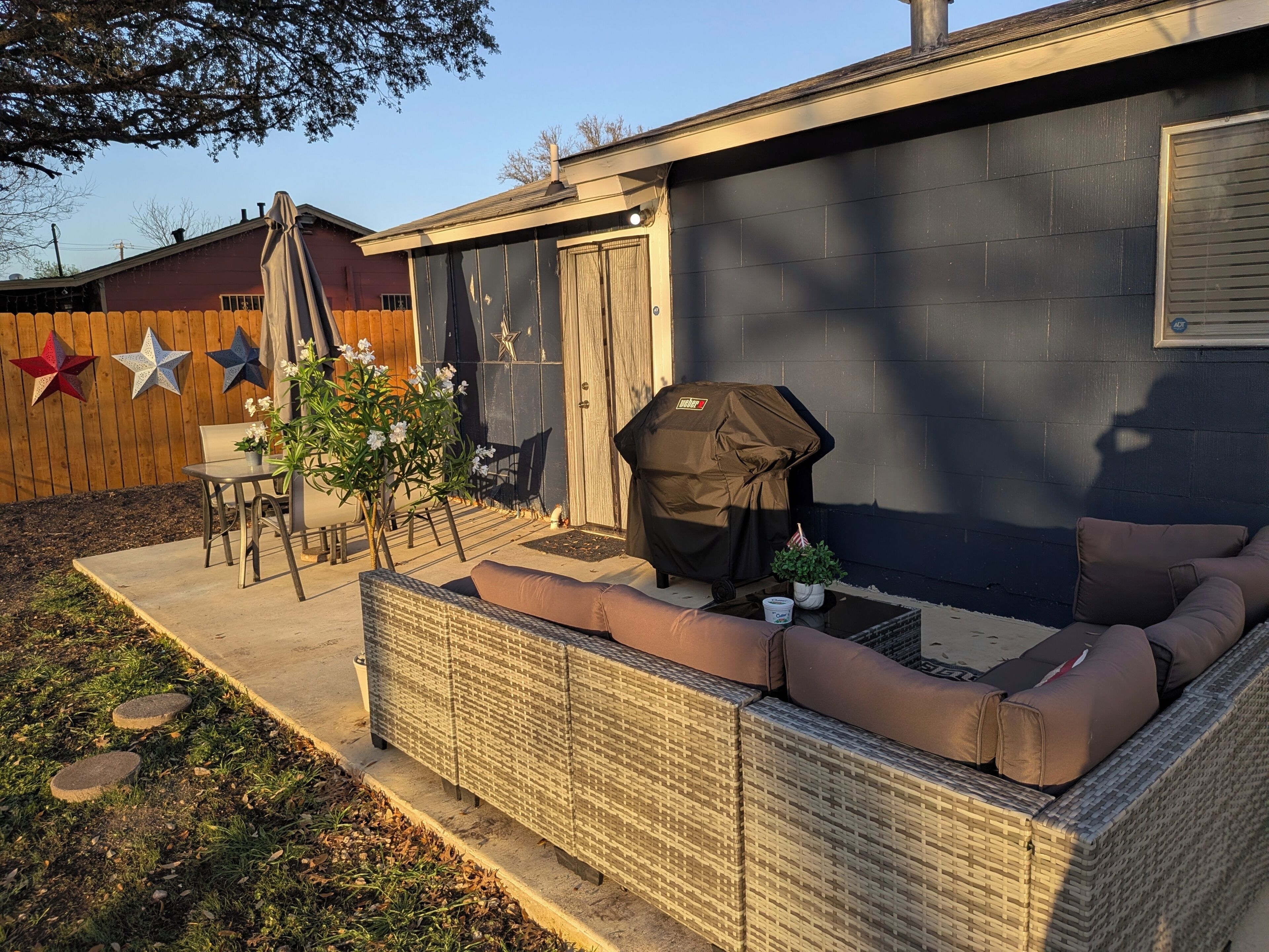 Een achtertuin met een overdekte barbecue, zitplaatsen buiten en een houten omheining.