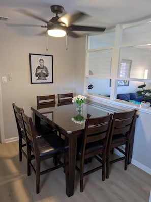 A dining area with a glass-top table, wooden chairs, a ceiling fan, and a framed picture on the wall. - Patriot's Post - just renovated near Lackland AFB (San Antonio)