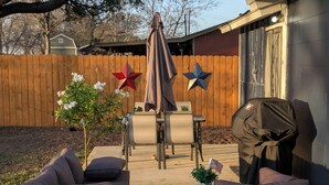 Un patio trasero con un sofá de mimbre, una mesa con sillas, una parrilla de barbacoa y estrellas decorativas en una valla de madera.