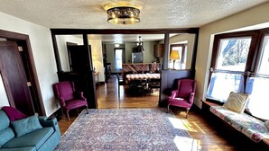 Un salon spacieux avec un grand tapis, deux fauteuils, un canapé et un coin repas à l’arrière-plan.