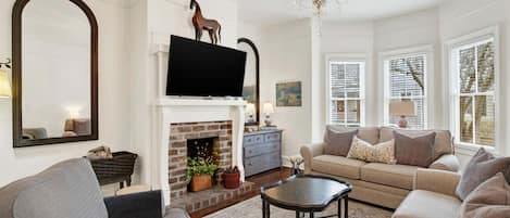 A living room with a fireplace, sofa, television, and chandelier.