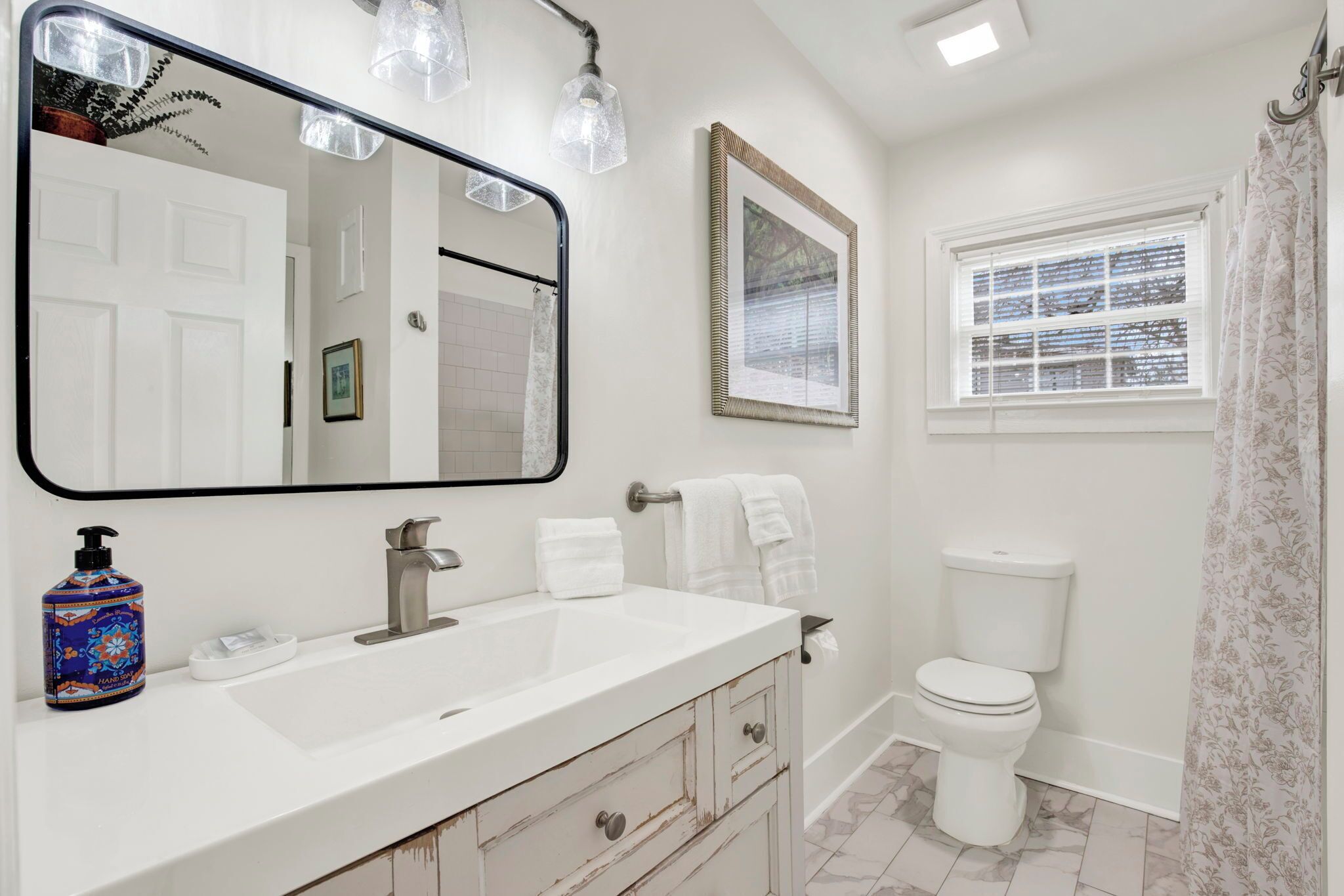 A bathroom with a large mirror, a white sink, a toilet, and a shower curtain.