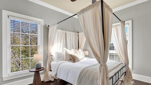 Camera da letto con un letto a baldacchino, una lampada da terra e vista su alberi attraverso una finestra con tende.