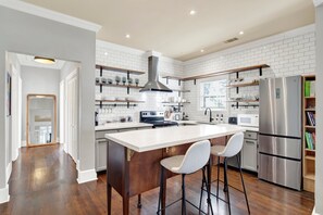 A modern kitchen with white subway tiles, stainless steel appliances, and wooden bar stools. - Southern Elegance in Historic Downtown Savannah | Heated Pool Access (Savannah)