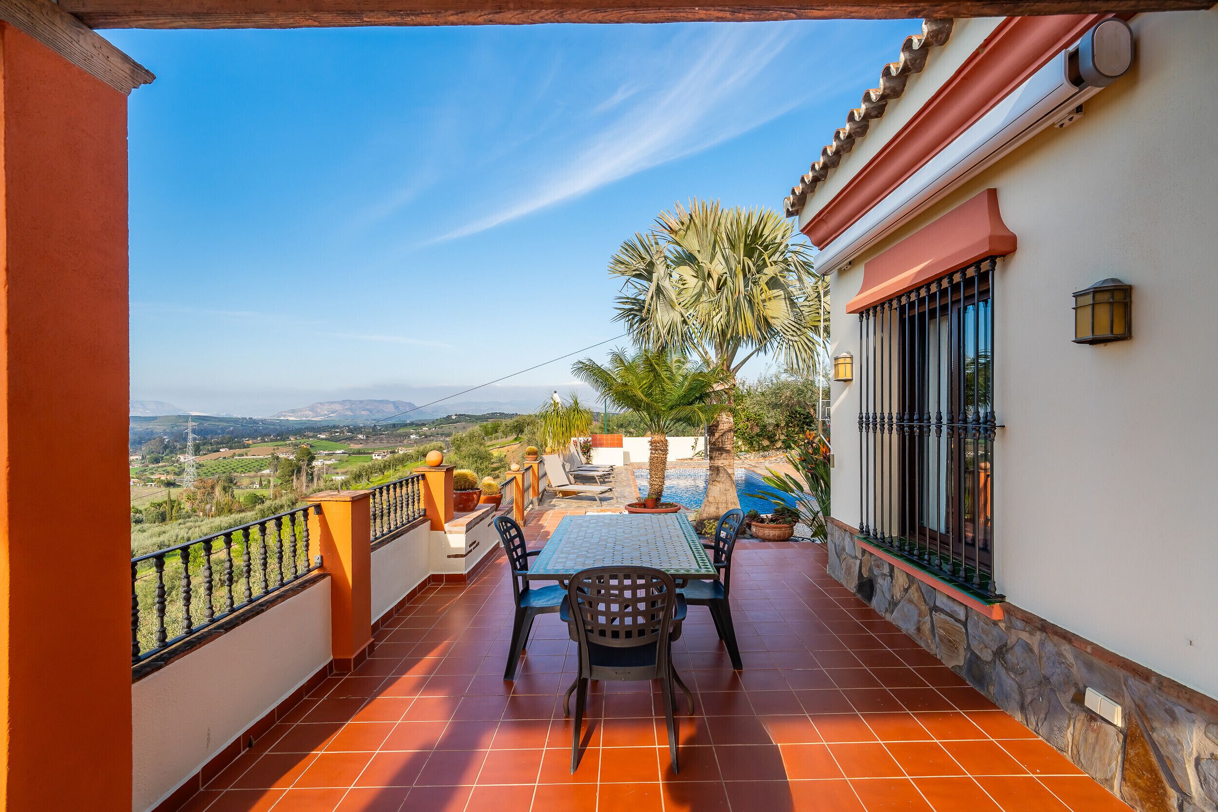 Un balcon avec une table et des chaises, offrant une vue panoramique sur un paysage magnifique, avec des montagnes et une piscine.