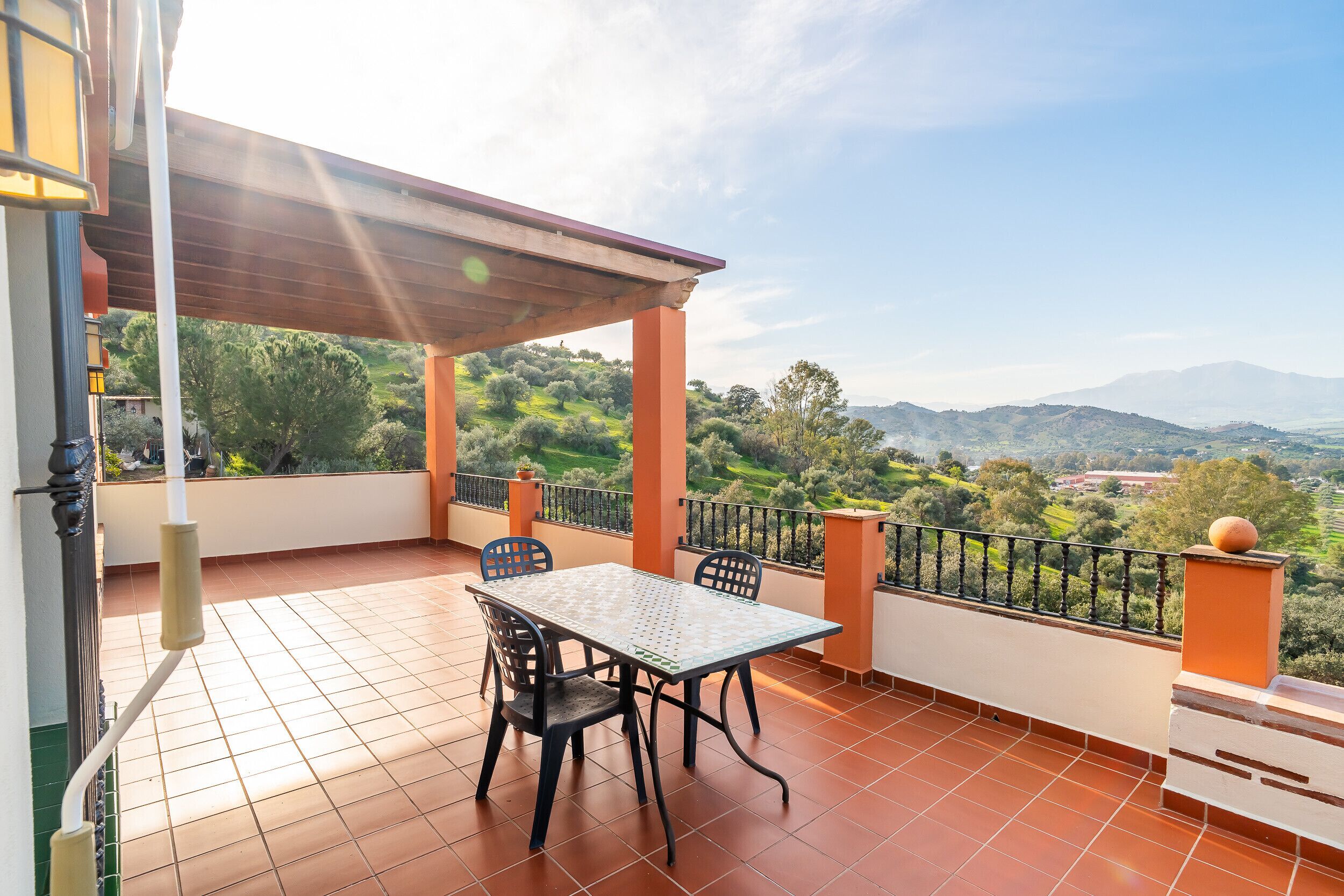 A terrace with a table and chairs, a pergola, and a view of the countryside.