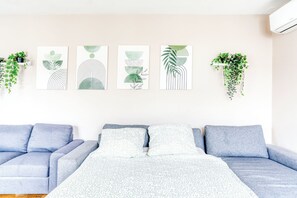 Une pièce avec un canapé bleu, un lit recouvert d’une couvre-lit à motifs et quatre œuvres d’art abstraites accrochées au mur.