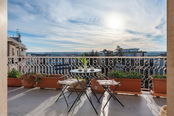 A terrace with a table and chairs, potted plants, and a view of the cityscape.