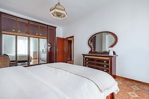 A bedroom with a large bed, wooden wardrobe, and a mirror.